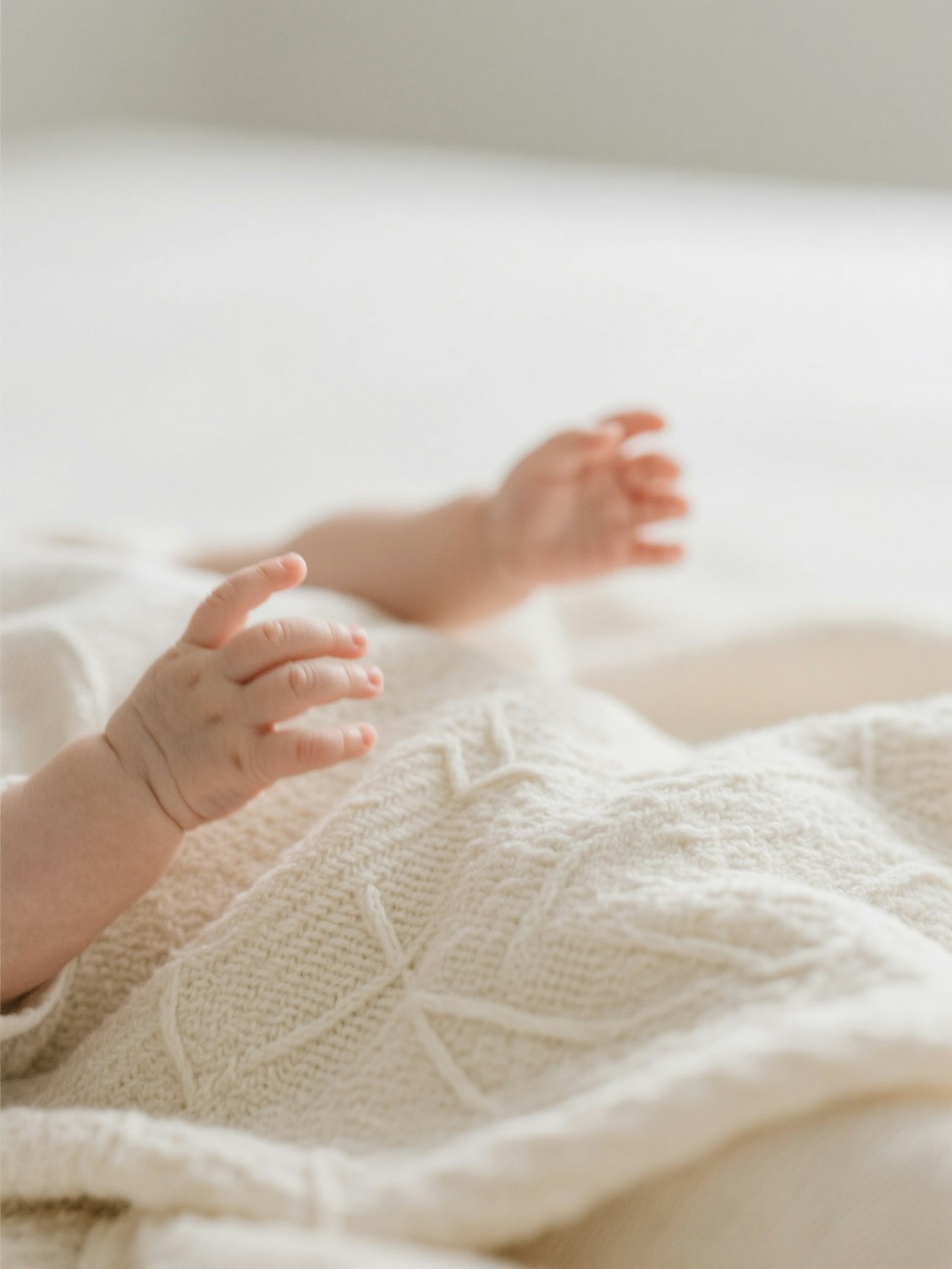 Baby hands resting on a cream crochet blanket with a raised vine pattern